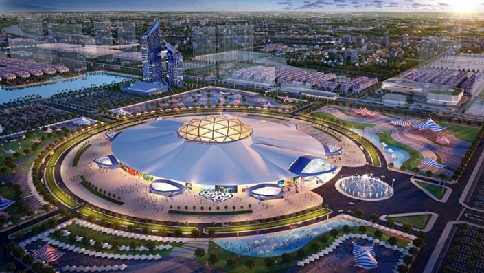 Toàn cảnh trung tâm hội nghị hoặc nhà thi đấu mái vòm lớn, hiện đại với quảng trường và cảnh quan xanh xung quanh.